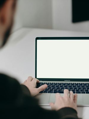 A man in a hoodie works on a blank-screen laptop at a clean, minimalist workspace indoor.